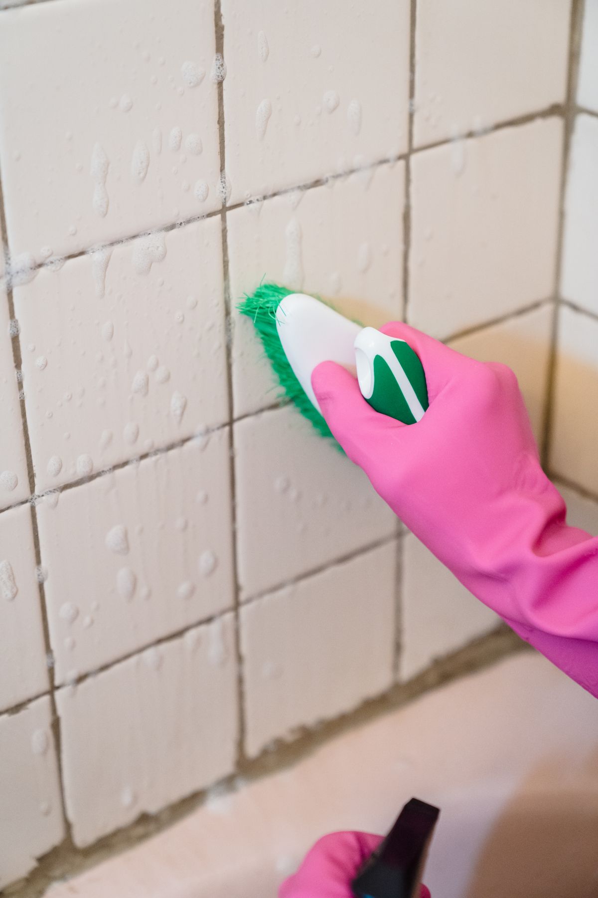 A gloved hand using a brush on bathroom wall tiles