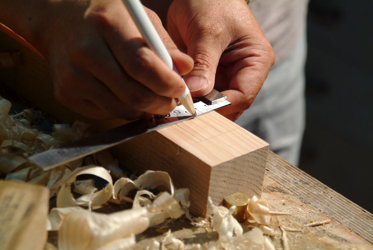 Hands marking a wooden plank with a pencil and ruler