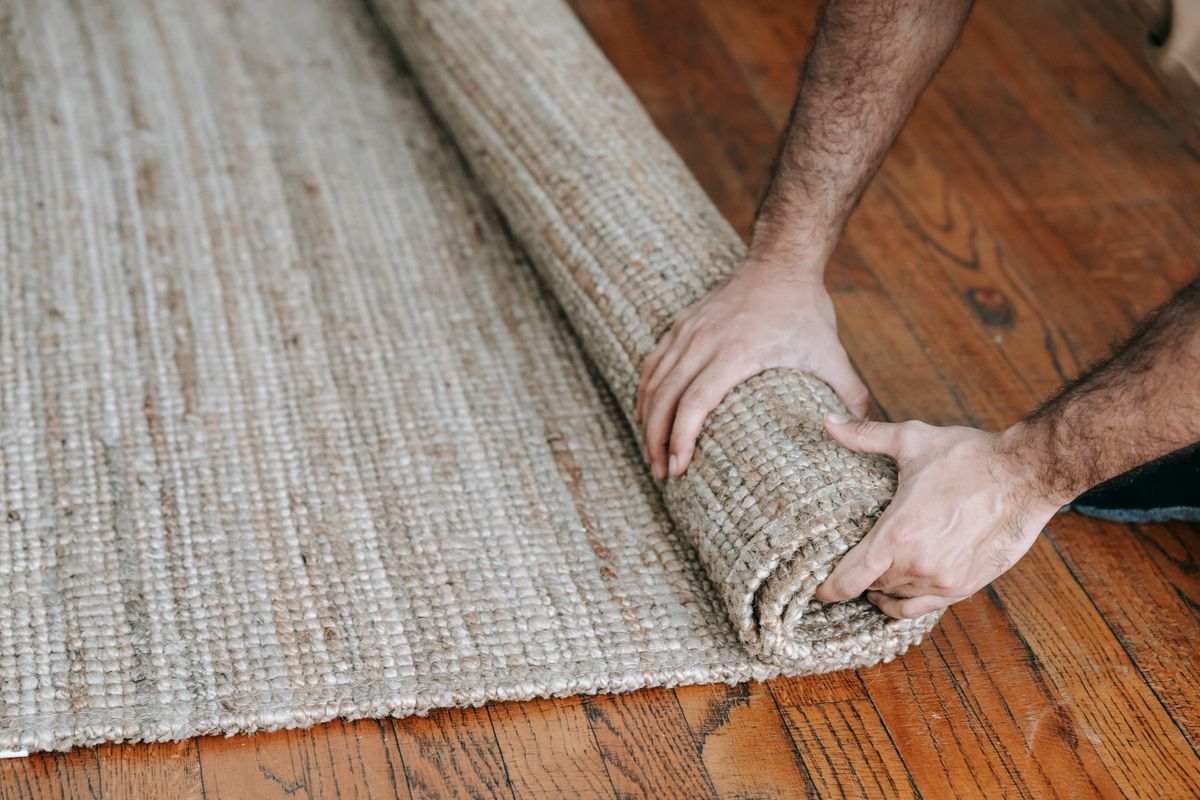 A person lifting and rolling a woven rug from the floor